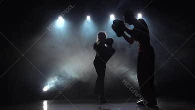Guy with a girl boxing gloves beating in the ring in the dark, they are preparing for a kickboxing competition