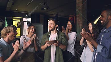 Slow motion of handsome bearded man blowing candles on birthday cake at office party with colleagues clapping hands and