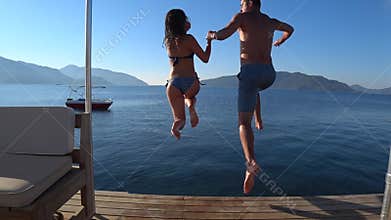 Summer vacation, happy friends with running start jump into sea from pier