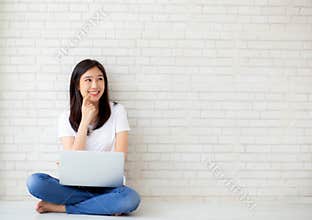 Beautiful of portrait asian young woman working online laptop and thinking sitting on floor brick cement background