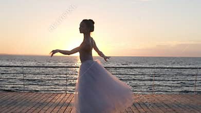Young beautiful woman is dancing wearing white tutu on sunrise or sunset. Performing classic ballet pas. Outdoors