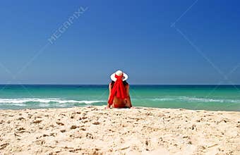 Woman in red bikini and hat sitting in peace on a beautiful sunny beach.