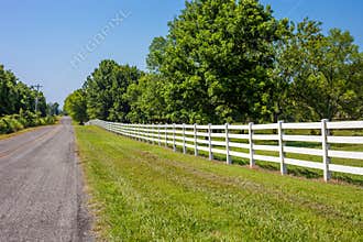 Empty countryside road with white fence and green trees
