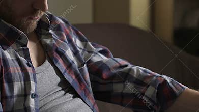 Drunk man in his 40s sitting on couch with beer bottle and sleeping, alcoholism