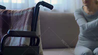 Disabled senior woman looking at wheelchair and thinking about health problems