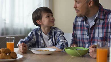 Pleased son and father eating tasty cornflakes at breakfast, morning tradition