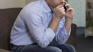 Sad male sitting on sofa and talking on cellphone with ex-girlfriend, crisis