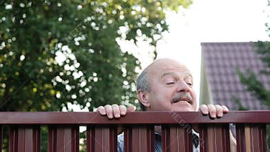 Senior man looking through fence spying on his neighbor.