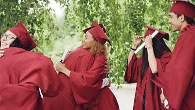 Slow motion of happy graduates wearing gowns and mortar-boards hugging, laughing and congratulating each other on
