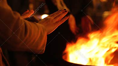 People warming hands near fire at street festival, winter holidays celebration