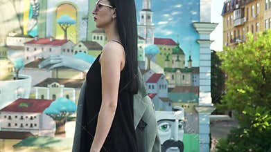 Stylish woman in black dress and sunglasses walk in slow motion against graffiti