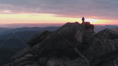 Drone shot of lonely man standing on top of a mountain and enjoying the sunset