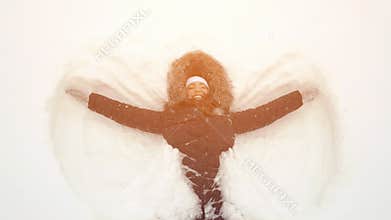 Happy girl lying on a snow and shows angel