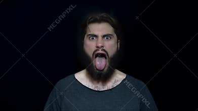 Young man with beard and tongue sticking out in rage. Angry young man to madness with open mouth. Human facial