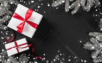 Creative layout frame made of Christmas tree branches, pine cones, gifts with red ribbon on dark background.