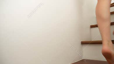 Close-up. The bare feet of a Caucasian woman climb to the top of the wooden stairs.