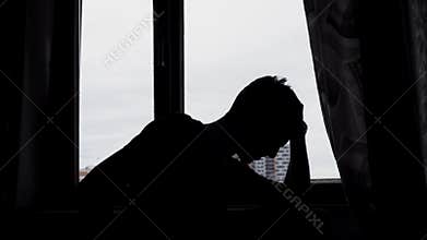 Silhouette of desperate sad man in the dark in front of a window