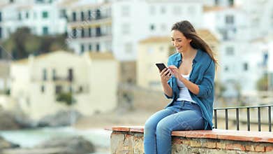 Happy woman browsing on phone on a ledge