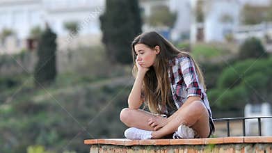 Bored teen complaining sitting on a ledge in a town
