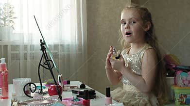 A little girl with red hair sprinkles perfume or toilet water, looks in the mirror, makeup, face, fashion, style
