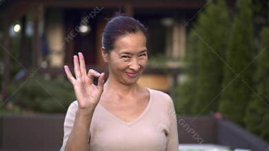 Middle aged asian woman showing ok sign outside