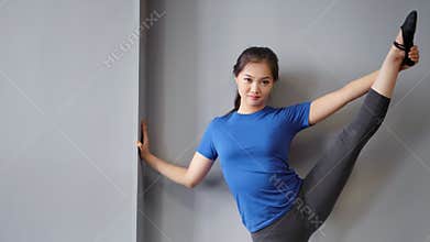 Smiling Asian female ballet dancer showing perfect stretching raising one leg holding by hand