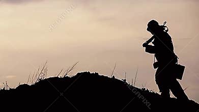 A traveler in a post-apocalyptic world sitting by the fire at sunset. Drink something then go over the hills in the background of