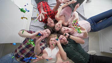 Friends with happy emotions playing with confetti lie together and smile at camera during a home party