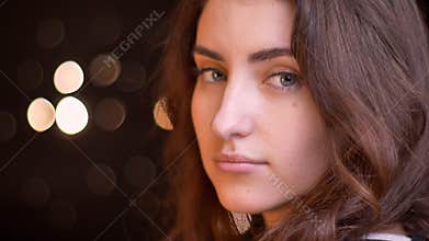 Closeup side view shoot of young attractive caucasian female face turning and looking at camera with bokeh lights on the
