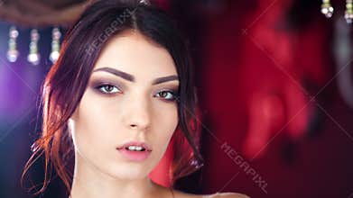 Close-up face of charming sensual young Caucasian woman posing at red lights background
