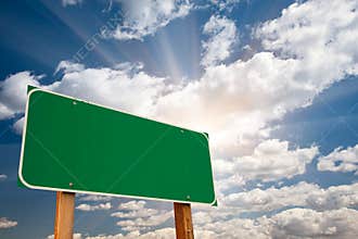 Blank Green Road Sign Over Clouds and Sunburst
