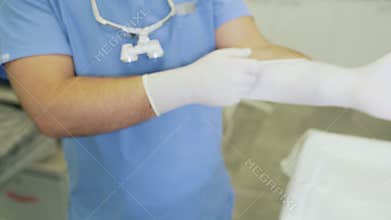 Close-up doctor in sterile clothing puts on gloves before surgery.