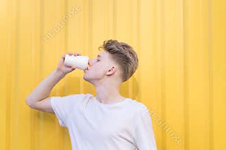 Portrait of a handsome man in blue t-shirt standing with coffee to go on the yellow backgroun