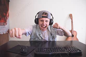 Joyfulmgamer playing video games at home on a computer. Gamer in headphones and cap is happy