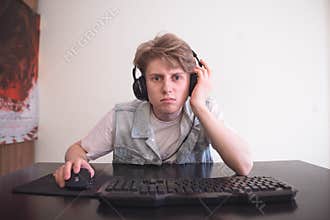 Sad teenage gamer sits at home behind a computer and plays video games