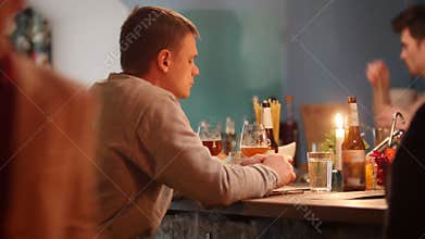Attractive sad man is sitting at the bar with soft interior lighting and drinking light beer while wating for someone.