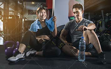 Fit people in exercise gear sitting together on the floor of a gym laughing together after a workout