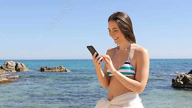 Girl in bikini checking smart phone on the beach