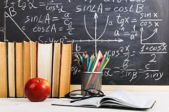 School desk in classroom, with books on background of chalk board with written formulas. Soncept Teacher`s Day