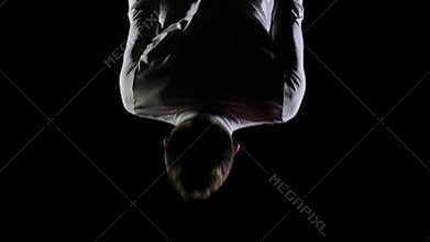 Young handsome male acrobat gymnast in white clothes on a black background makes jumps and shows tricks with rotation