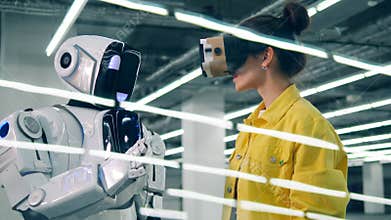 One woman touches robot`s hand while wearing VR glasses.