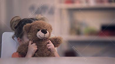 Sad female kid covering face by teddy bear toy, family problem, loneliness abuse