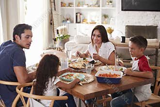 Young Hispanic family sitting at dining table eating dinner together
