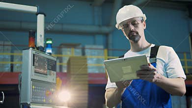 Plant worker types on a tablet, standing in a facility room.