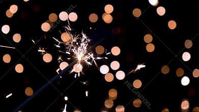 Sparkler burning in front of ambient lights in slow motion