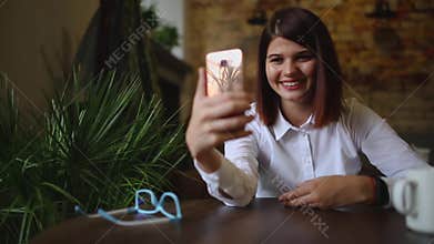 Smiling girl in cafe talking on the video chat on smart phone while drinking coffee