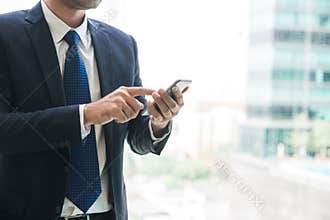 Businessman using mobile phone app texting outside of office in urban city with skyscrapers buildings in the background.
