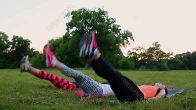 Feeling your abs girls. Group of young athletic people in sportswear doing physical exercises on green grass in summer