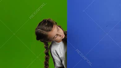 Child looks out from behind the blue board and laughs. Green screen