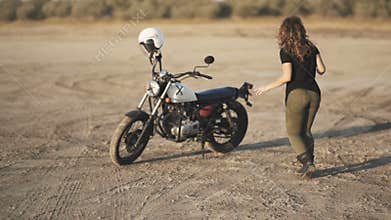 Young beautiful woman dances in the desert at sunset or sunrise and then sits on a motorcycle and ride away